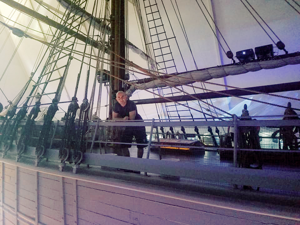 A man poses on a model ship on display at a museum 