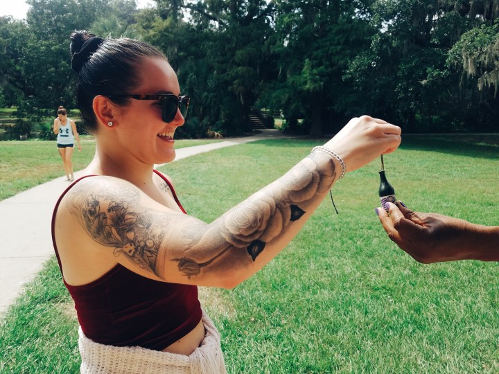 A woman with sunglasses and tattoos and a red tank top dipping a bubble wand into a small tube of bubbles as part of the Champagne Destiny Reading.