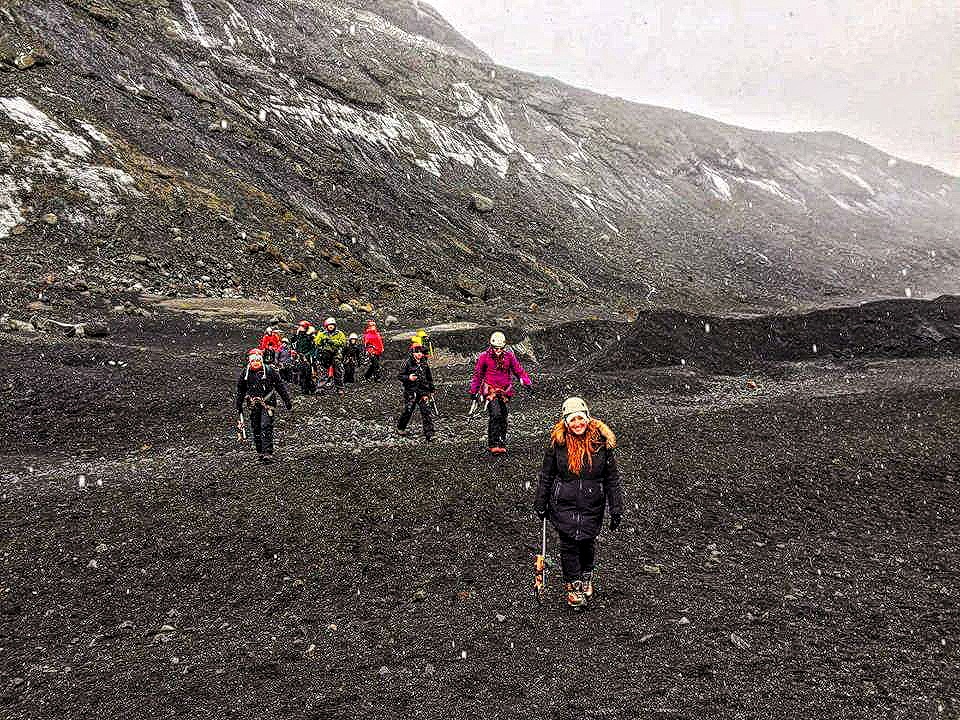 A group of people walk across a valley of ash to get to Solheimajokull glacier