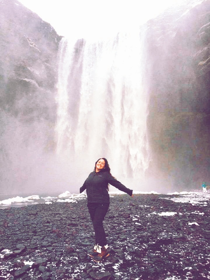 A woman stands at the base of a waterfall in Iceland