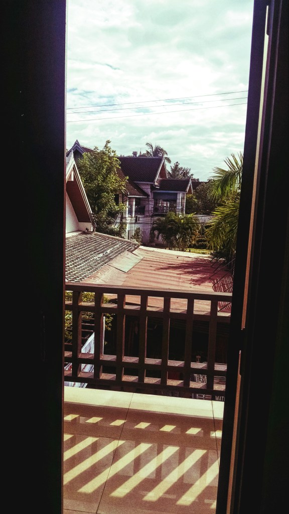 The beautiful view outside of a Luang Prabang hotel room - palm trees and a light blue sky. One of the many ways how I fell in love with Laos